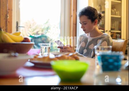 Édimbourg, Écosse, Royaume-Uni. Janvier 2021. Une fille de 12 ans regardant son smartphone à la table du petit déjeuner Banque D'Images