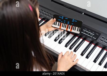 Une petite fille apprend à jouer le piano à partir de leçons vidéo. Apprentissage à distance en ligne pendant le Covid-19 Banque D'Images