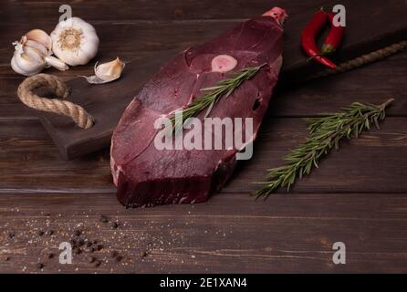 viande fraîche crue sur fond de bois. venaison au poivron rouge et au romarin. ail et assaisonnements. cuisson d'une délicieuse viande de cerf. Banque D'Images