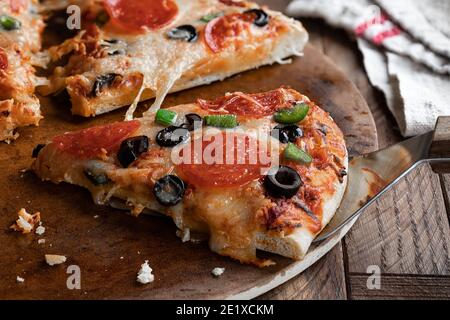 Gros plan d'une tranche de pizza avec du pepperoni, des olives et des poivrons verts sur une pierre à pâtisserie Banque D'Images