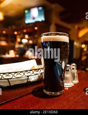 Verre de bière foncée sur une table dans un pub réglage Banque D'Images