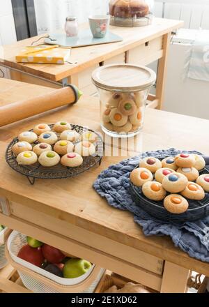 Deux casiers de refroidissement avec beaucoup de cookies colorés sur eux. Un pot transparent avec beaucoup de cookies à l'intérieur est entre eux. Une autre table en bois avec Banque D'Images