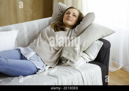 Bonne femme brunette a mis les mains derrière la tête allongé sur le canapé une femme européenne Profitez d'un week-end paresseux ou de vacances dans le salon confortable, femme au foyer Banque D'Images