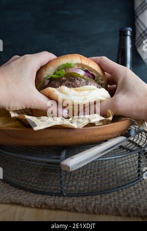 Hamburger de bœuf fait maison étant tenu par des mains de femme prêtes à être dévorées. Banque D'Images