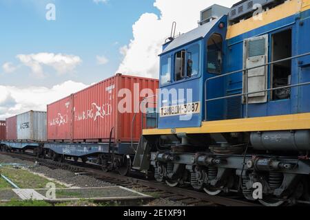 Une locomotive avec un conducteur dans la cabine dans le cadre d'un train de marchandises avec des conteneurs se tient sur la voie de chemin de fer par une journée ensoleillée d'été. Banque D'Images