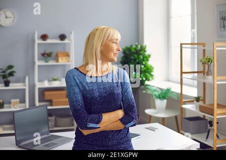 Bonne femme pensive mature dans l'habillement décontracté debout bras croisés et regarder loin Banque D'Images