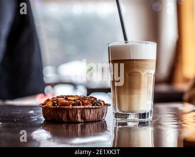 Café Latte chaud dans un verre et dessert aux pommes fraîches à côté. La boisson chaude est servie avec une paille en plastique. Délicieux petit déjeuner au café Banque D'Images