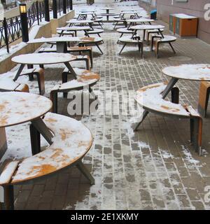 Des tables et des bancs couverts de neige se trouvent sur la rue de la ville, sur un trottoir à côté du restaurant McDonald's Winter en Russie. Banque D'Images