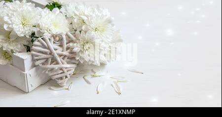 Bouquet de chrysanthèmes blancs, coeur en paille sur fond blanc scintillant. Motif carte pour le jour de la Saint-Valentin ou le jour de la mère. Banque D'Images