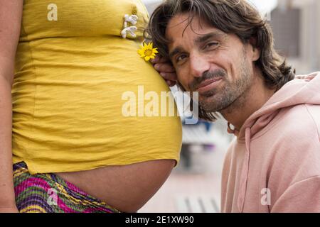 Fier papa se penche la tête sur la mère enceinte qui tient la fleur jaune. Un père ravie attend un nouveau membre de sa famille. S'attendre à des parents, la santé des femmes Banque D'Images