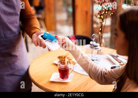 Photo d'une femme assise à un bureau dans le café et payant avec une carte de crédit. Paiement sans contact. Banque D'Images