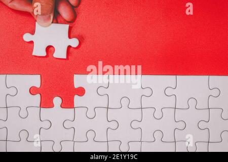 Doigt humain touchant des pièces de puzzle blanc non finies sur le rouge arrière-plan de l'objectif de fin