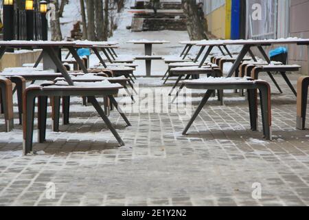 Des tables et des bancs couverts de neige se trouvent sur la rue de la ville, sur un trottoir à côté du restaurant McDonald's Winter en Russie. Banque D'Images