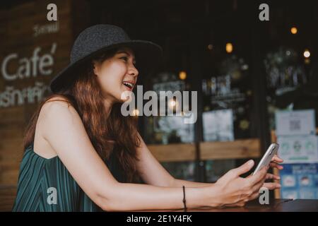 Jeune belle femme asiatique travaillant dans un café loft ou un bureau. Tenir le smartphone pour naviguer sur Internet et effectuer des recherches wi-fi. Femme d'affaires ou pigiste Banque D'Images