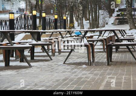 Des tables et des bancs couverts de neige se dressent sur la rue de la ville, sur un trottoir à côté du restaurant Winter en Russie. Banque D'Images