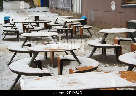 Des tables et des bancs couverts de neige se dressent sur la rue de la ville, sur un trottoir à côté du restaurant Winter en Russie. Banque D'Images