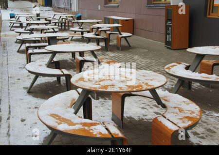 Des tables et des bancs couverts de neige se dressent sur la rue de la ville, sur un trottoir à côté du restaurant Winter en Russie. Banque D'Images