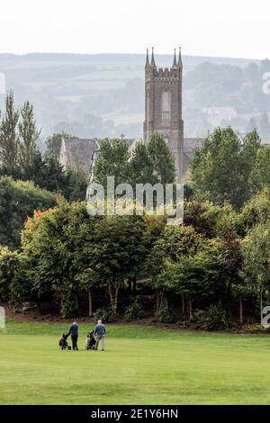 Deux hommes jouant au golf sur le parcours Citywest Hotel Golf Club avec l'église de la Nativité de la Sainte Vierge Marie en arrière-plan. Dublin, Irlande. Banque D'Images