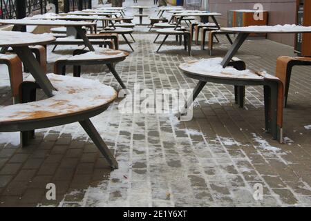 Des tables et des bancs couverts de neige se dressent sur la rue de la ville, sur un trottoir à côté du restaurant Winter en Russie. Banque D'Images