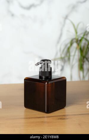 Bouteille de pompe carrée en verre ambré maquette sur table dans la salle de bains. Design élégant de l'emballage du distributeur de savon. Banque D'Images