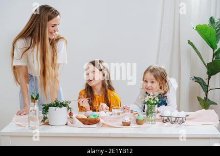 Une jeune mère avec ses deux filles peignant derrière elle des œufs de pâques une table Banque D'Images