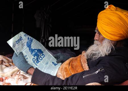PORTRAIT D'UN MANIFESTANT D'AGRICULTEURS LISANT UN ARTICLE À LA FRONTIÈRE DE DELHI , ILS PROTESTENT CONTRE LA NOUVELLE LOI AGRICOLE ADOPTÉE PAR LE GOUVERNEMENT INDIEN. Banque D'Images