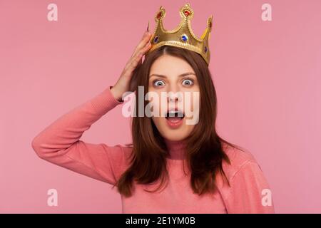 Gros plan choqué femme bossy avec les cheveux bruns dans le chandail rose ajustement couronne dorée sur la tête regardant la caméra avec les grands yeux et la bouche ouverte. Goujon intérieur Banque D'Images