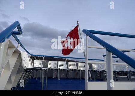 Drapeau fédéral suisse, rouge avec croix blanche, qui souffle dans le vent au-dessus du lac de Zurich sur un bateau de croisière sur le lac. Banque D'Images