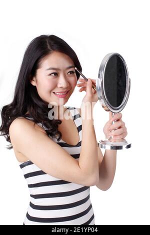 Jeune femme dans une robe rayée regardant dans un miroir, application maquillage photo de haute qualité Banque D'Images