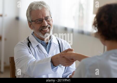 Un vieux médecin souriant se secouant la main avec une jeune patiente. Banque D'Images