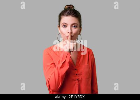 Garder le silence ! Portrait de femme élégante avec bun hairstyle, big earrings et en rouge en chemisier humble geste avec le doigt sur les lèvres, pour demander la société Banque D'Images