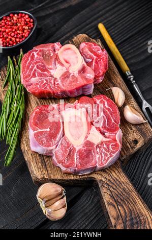 Viande crue Osso buco bœuf de veau, faire de l'Ossobuco italien. Arrière-plan en bois noir. Vue de dessus Banque D'Images