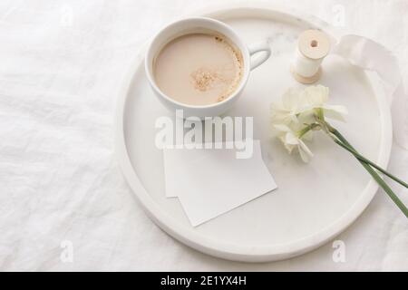Mariage de printemps encore la vie. Maquettes de cartes de visite. Ruban de soie, narcisse jonquilles fleurs sur plateau en marbre. Tasse de café avec lait. Table en lin blanc Banque D'Images