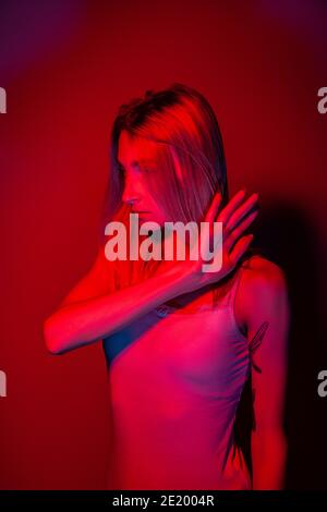 Femme anonyme couvrant le visage avec la main dans une lumière rouge au néon Banque D'Images
