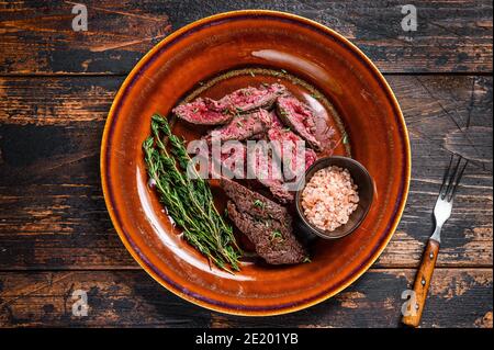 Filet d'onglet grillé moyen rare suspendu de viande tendre steak de bœuf sur une assiette. Arrière-plan en bois sombre. Vue de dessus Banque D'Images