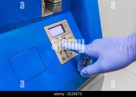 La main d'un homme dans des gants médicaux de protection compose un code PIN au terminal pour émettre de l'argent, gros plan. Banque D'Images