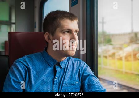 Jeune européen en chemise bleue, regardant par la fenêtre d'un train électrique moderne en voyage. Banque D'Images