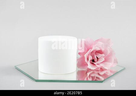 Pot blanc à cosmétiques vierge et fleur rose sur miroir, fond gris. Natural Organic Spa Cosmetic Beauty concept maquette, vue de face. Banque D'Images