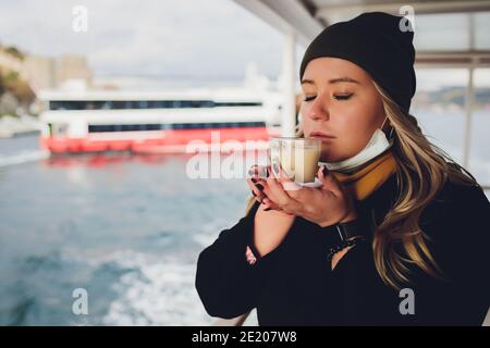 La main d'une femme tient une tasse blanche de chaud boisson lactée à la cannelle appelée sahlep de salep turc sur le Fond de l'eau ondulée et de la brumeuse Ma Banque D'Images