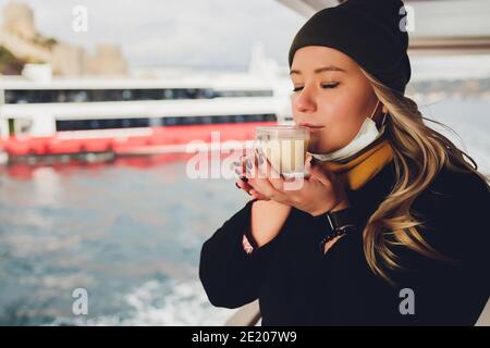 La main d'une femme tient une tasse blanche de chaud boisson lactée à la cannelle appelée sahlep de salep turc sur le Fond de l'eau ondulée et de la brumeuse Ma Banque D'Images