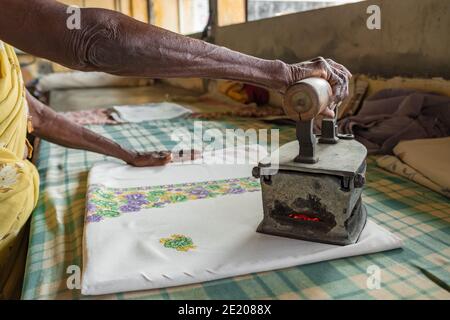 Femme sénior non-dentifiée repassant des vêtements avec un vieux charbon chauffé le fer en Inde Banque D'Images
