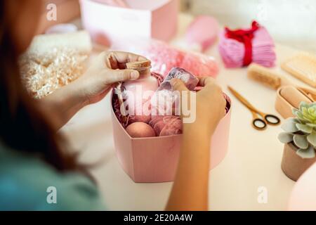 Femme préparant des boîtes-cadeaux en forme de coeur de couleur rose avec bio cosmétiques naturels de soins du corps Banque D'Images