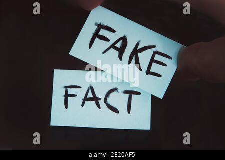 Fait ou faux concept, changement. Substitution de concepts. Le fait est remplacé par un faux. Un homme change les signes avec les mots fait sur faux sur un noir Banque D'Images
