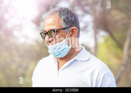 Portrait homme âgé seul voyageur porte un masque et voyage dans une forêt. Le vieil homme porte un masque facial, de la mauvaise façon, l'usure incorrecte - les masques devraient couvrir le nez. Banque D'Images