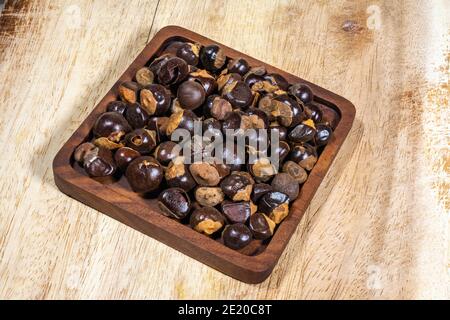 Guarana (Paullinia cupana) graines dans un bol en bois plat sur une planche à bois Banque D'Images