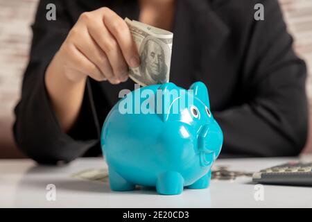 Gros plan une femme d'affaires de la main mettant l'argent billet de banque dollar dans un piggy. Économiser de l'argent richesse et concept financier. Banque D'Images