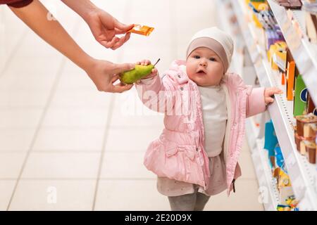 Shopping. Portrait de l'enfant mignon est debout près de l'étagère avec des produits, et choisira entre un bonbon et une poire, que la maman offre. Le concept o Banque D'Images