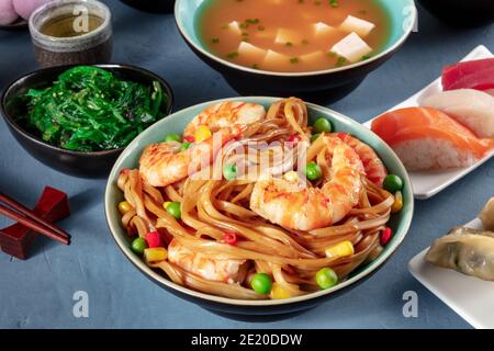 Dîner japonais. Nouilles sautées aux crevettes, soupe miso, nigiri, wakame, thé vert sur fond bleu Banque D'Images