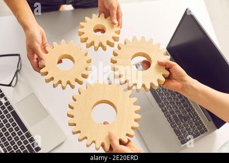 Gros plan des mains de jeunes entrepreneurs startups attacher des engrenages en bois les uns aux autres sur le bureau dans le bureau. Banque D'Images