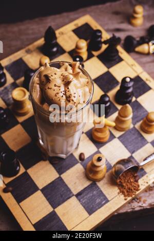 Café Dalgona. Boisson fouettée à glacer avec café instantané populaire en Corée cocktail crémeux dans de grands verres décorés d'échecs sur chessboard en bois Banque D'Images